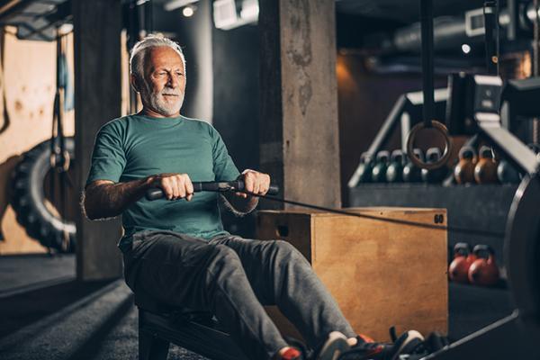 A senior man exercises using a rowing machine in a gym.