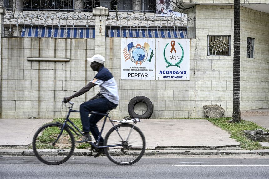 A cyclist rides past a PEPFAR sign in Abidjan, Ivory Coast, in July 2025.