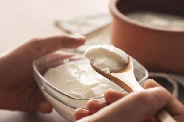 Close-up of hands holding a glass bowl of yogurt and a spoon.