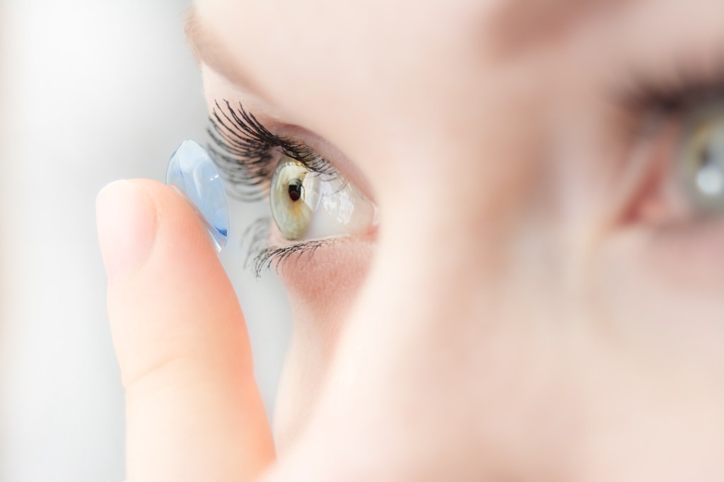 Close-up of a person's eye as they insert a soft blue contact lens with their finger.