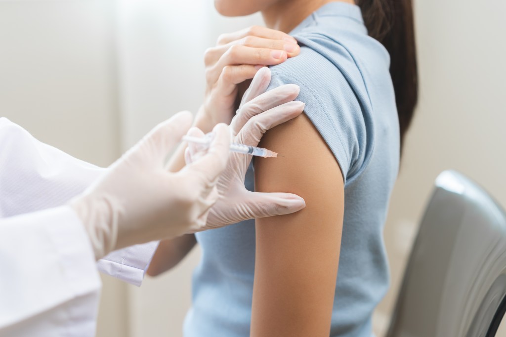 A gloved hand administering an injection with a syringe into a patient's arm.