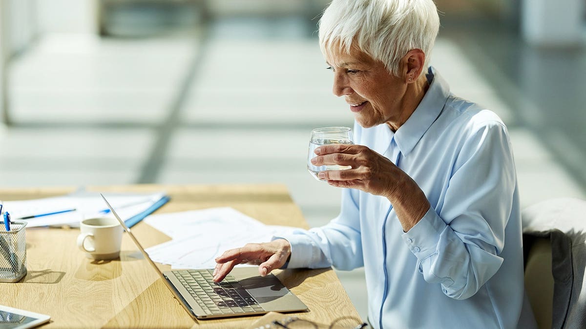 Female entrepreneur drinks water while working on a computer in an office.