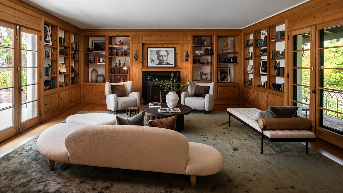 A wood-paneled library contains bookshelves, seating and a fireplace.