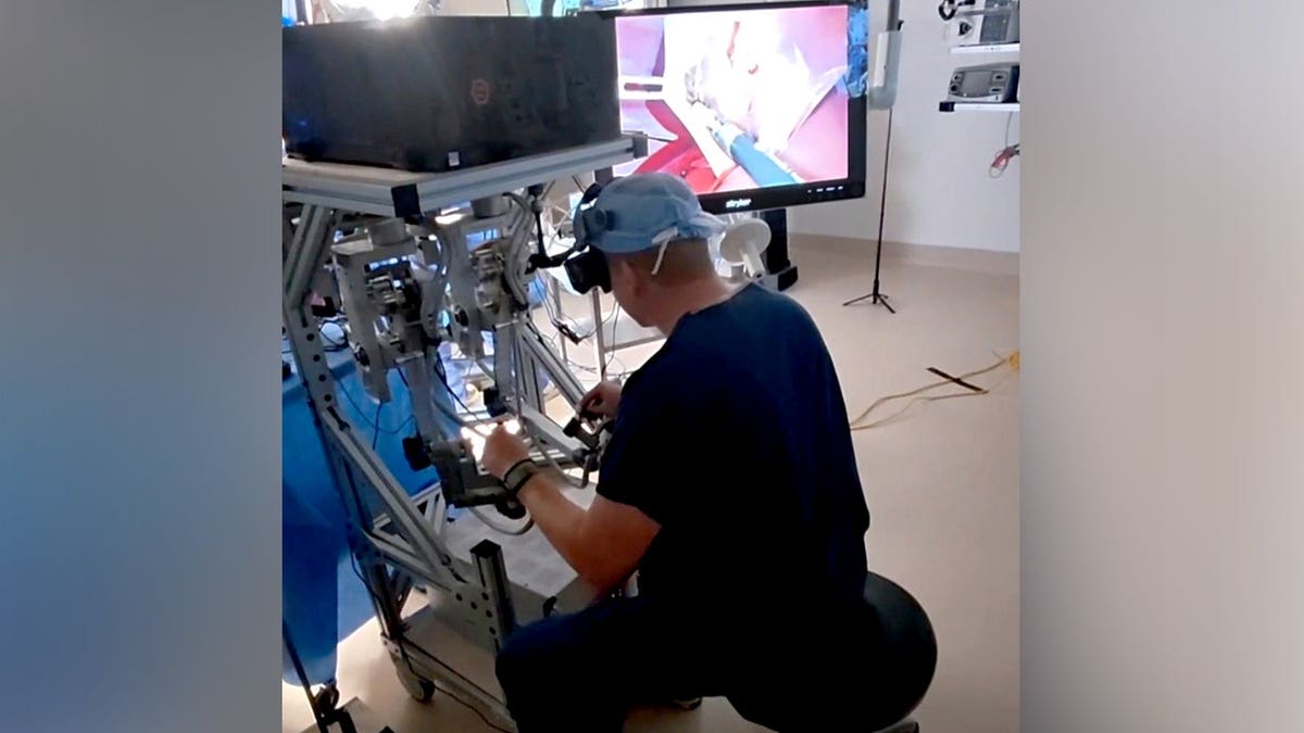 A surgeon uses a remote console to guide a humanoid robot during a surgery.