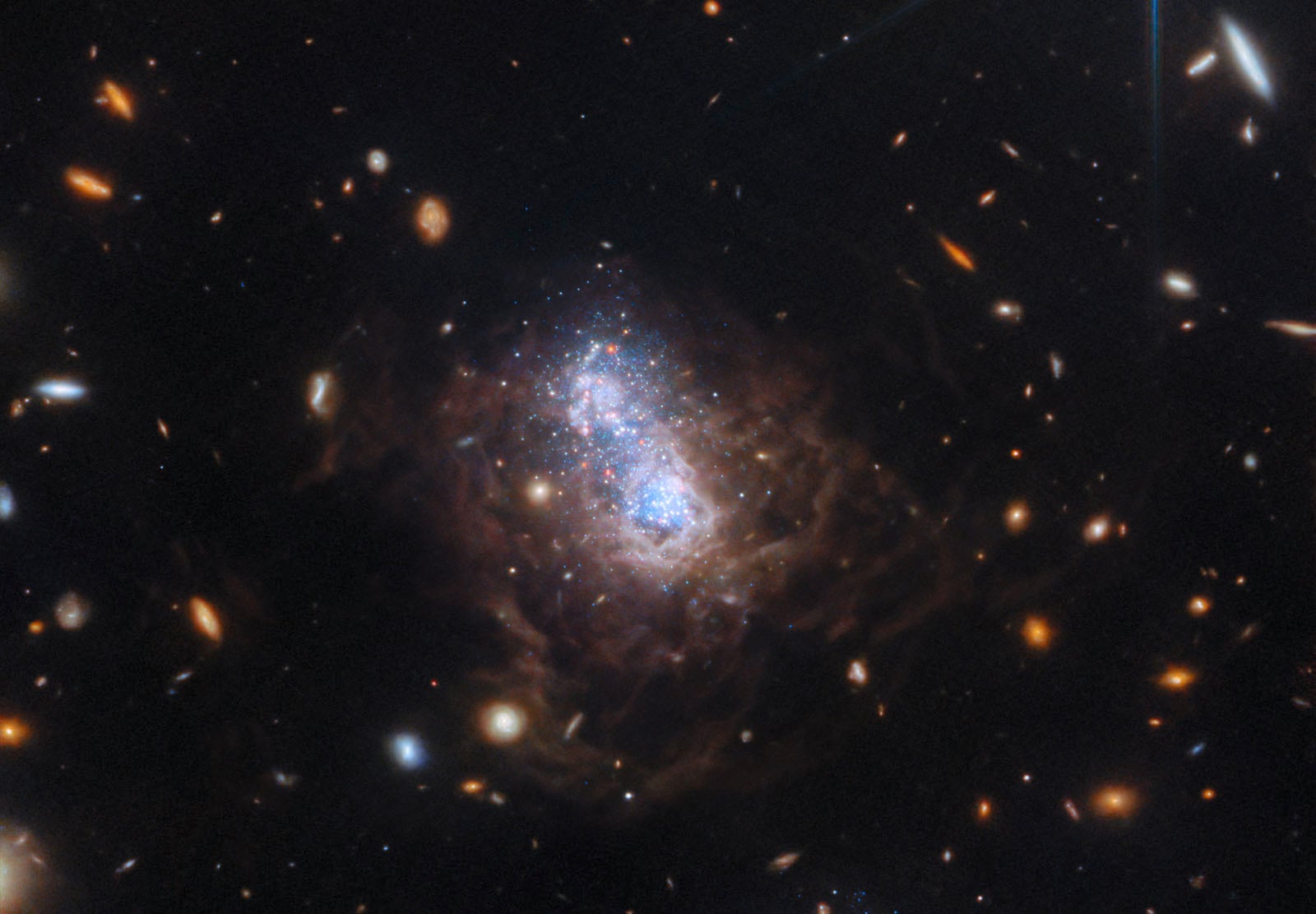 A bright blue galaxy glows at the center, surrounded by swirling clouds of dust and distant, scattered stars and galaxies against the dark backdrop of space.
