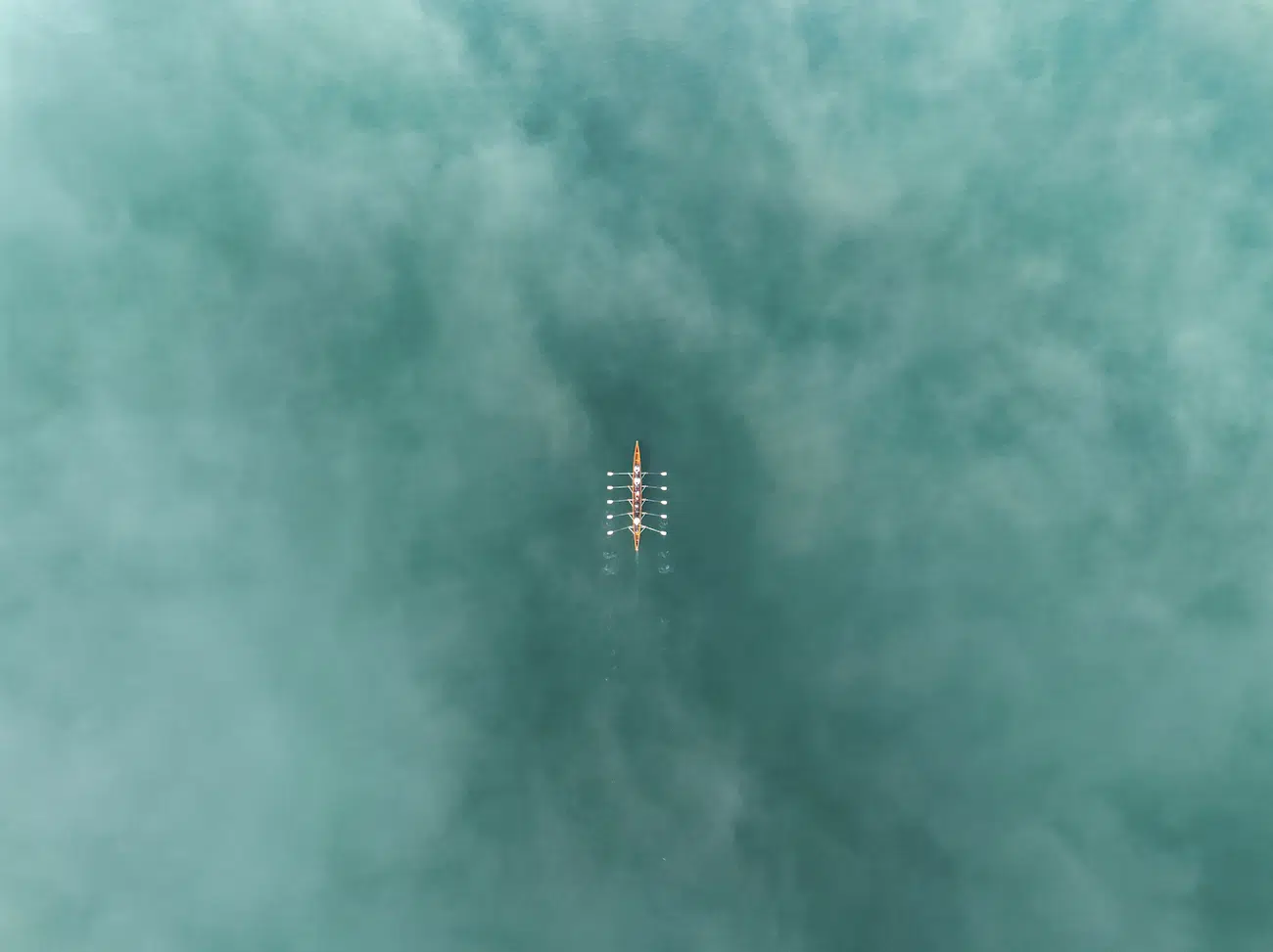 Azim Khan Ronnie, Bangladesh. Gliding through Serenity. An aerial view of a rowing team gliding through the pristine waters of Lake Zurich in Switzerland. The team is perfectly synchronized, with oars cutting cleanly into the turquoise, misty surface, leaving subtle ripples in their wake.