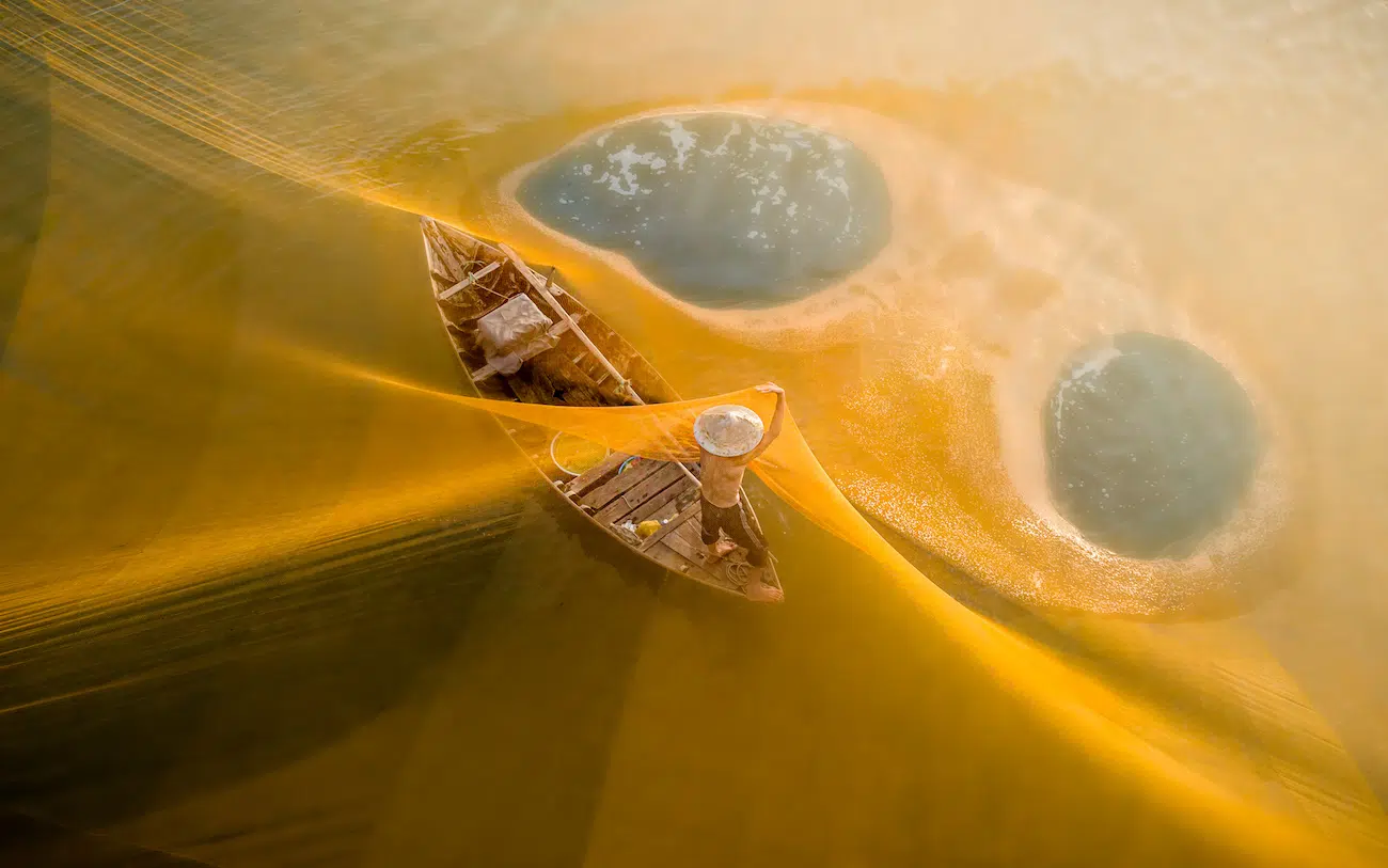 Chin Leong Teo, Singapore. Dawn Net. A lone fisherman casts a radiant yellow net that blooms across the water like liquid sunlight. From above, the sweeping lines wrap around his small boat, turning a simple act into a moment of quiet poetry.