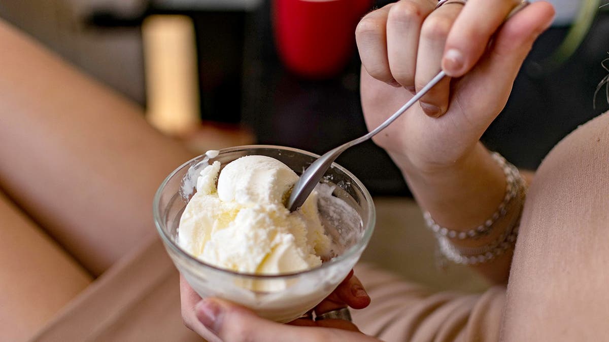 A woman holds a bowl of ice cream with a spoon in it.