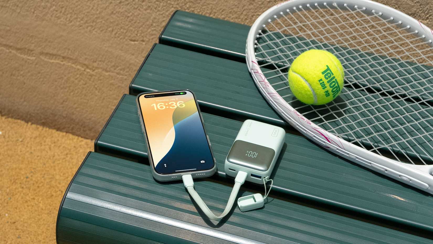 The INIU Pocket Rocket P50 charging a phone beside a tennis racket and ball