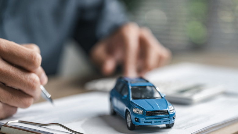 A visualization of a car payment with someone signing a contract and a toy car on the page.