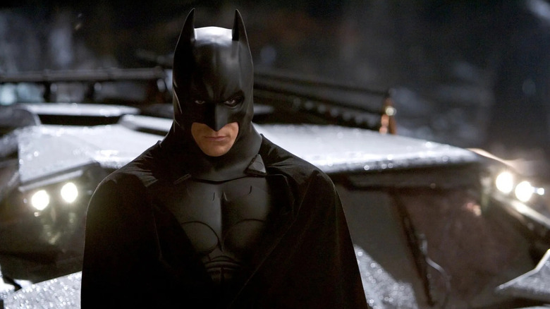 Bruce Wayne brooding next to the batmobile in Batman Begins