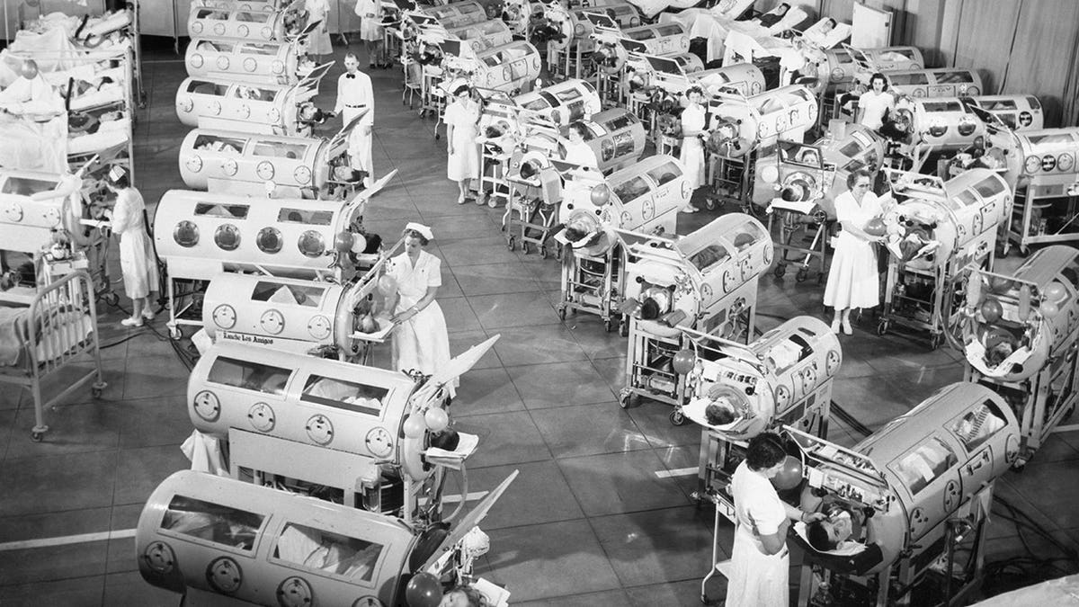 Iron lungs line up in a hospital room.