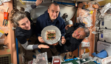 From left, Expedition 74 flight engineers Anna Kikina and Pyotr Dubrov of Roscosmos, and Anil Menon of NASA pose for a portrait while holding a cake celebrating their recent arrival aboard the International Space Station.