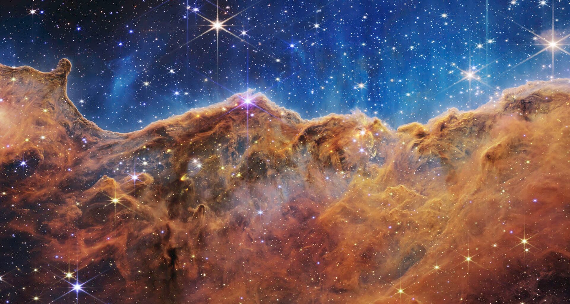 Colorful nebula with bright stars scattered across a vivid blue and orange cosmic cloud, resembling a mountainous landscape in outer space.