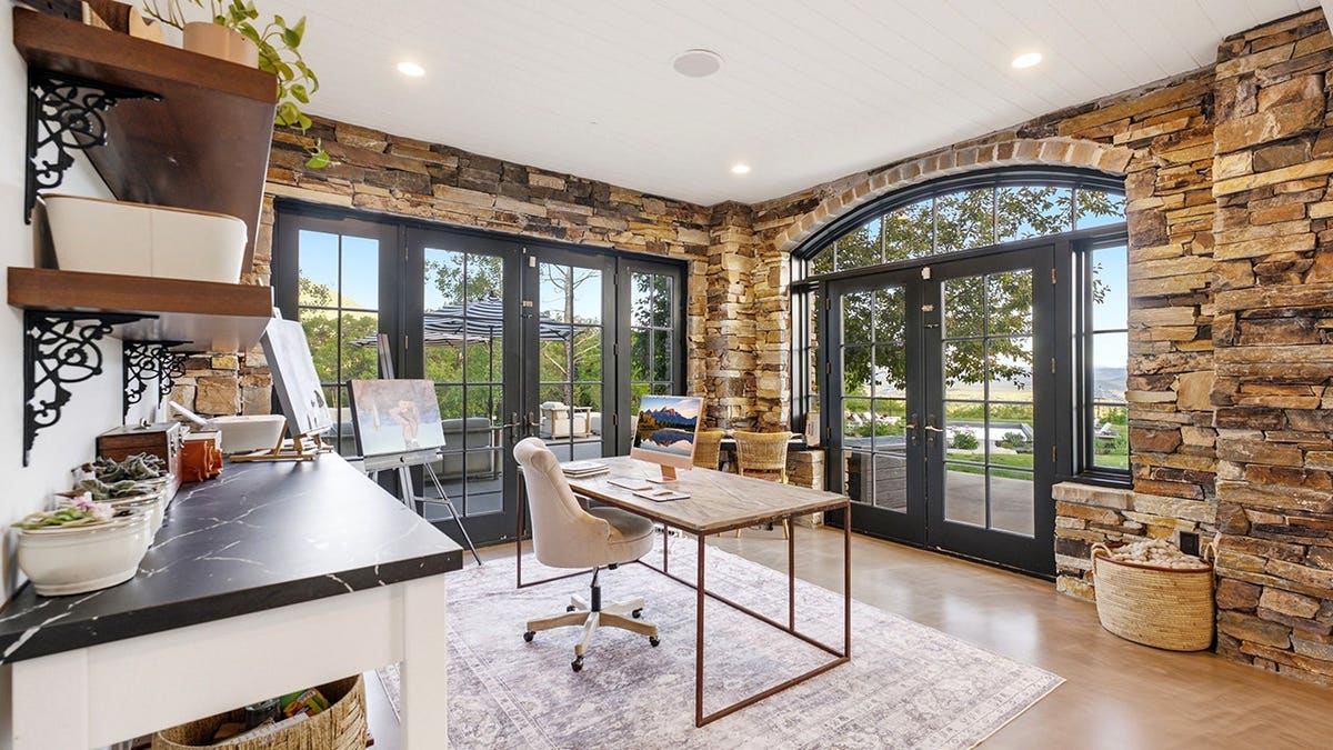 A home office with stone walls and a double door leading outside.