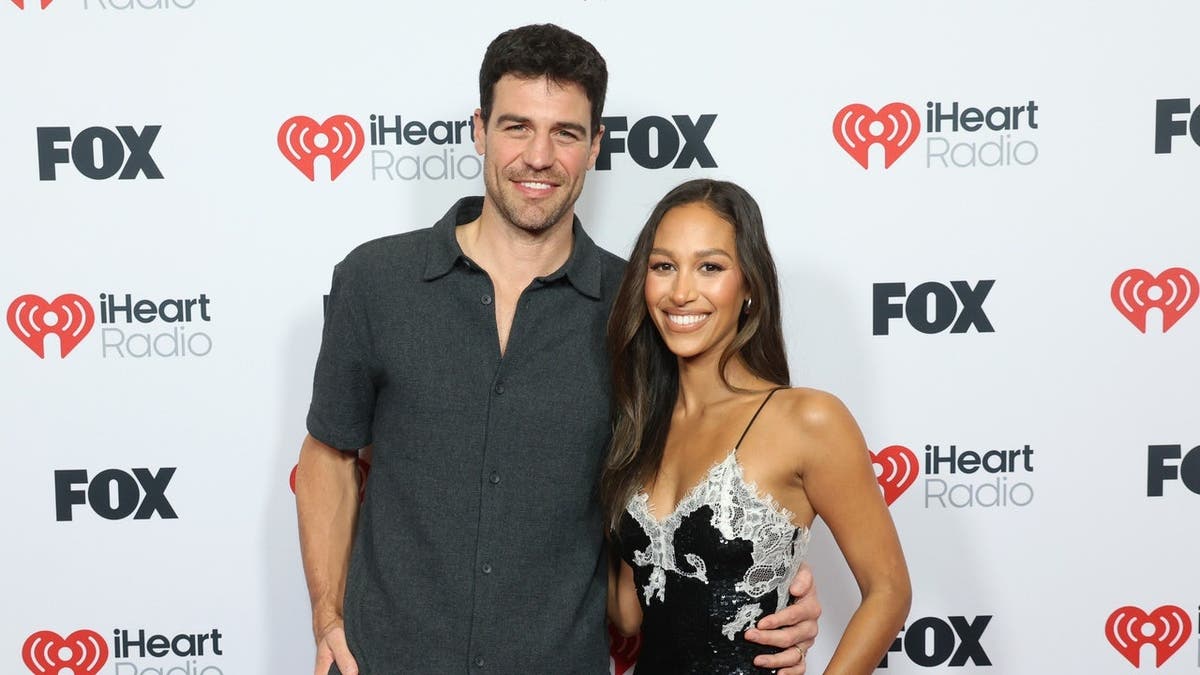 Joe Amabile and Serena Pitt stand together at the iHeartRadio Music Awards press room.
