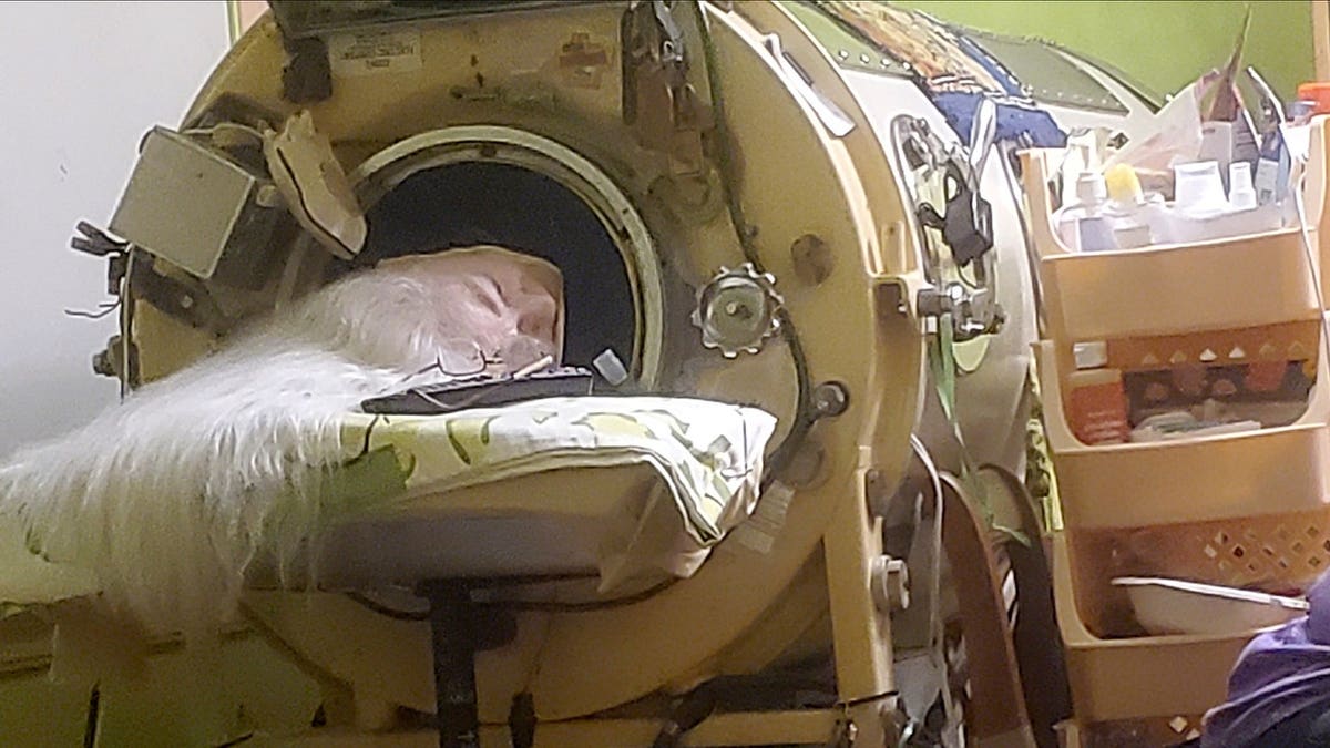 Martha Lillard rests in an iron lung in a room.