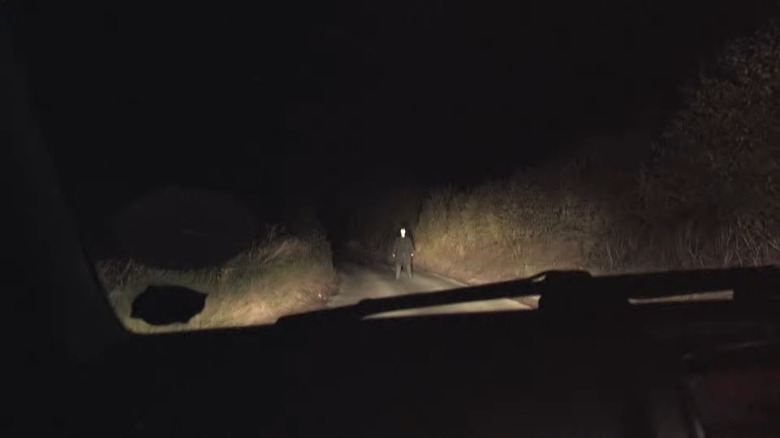 A car approaches a figure on the road in No Through Road.