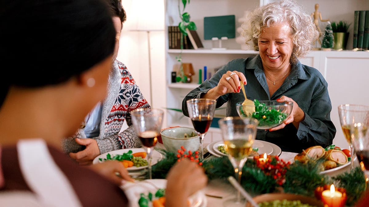 An older woman smiles while enjoying dinner with friends.