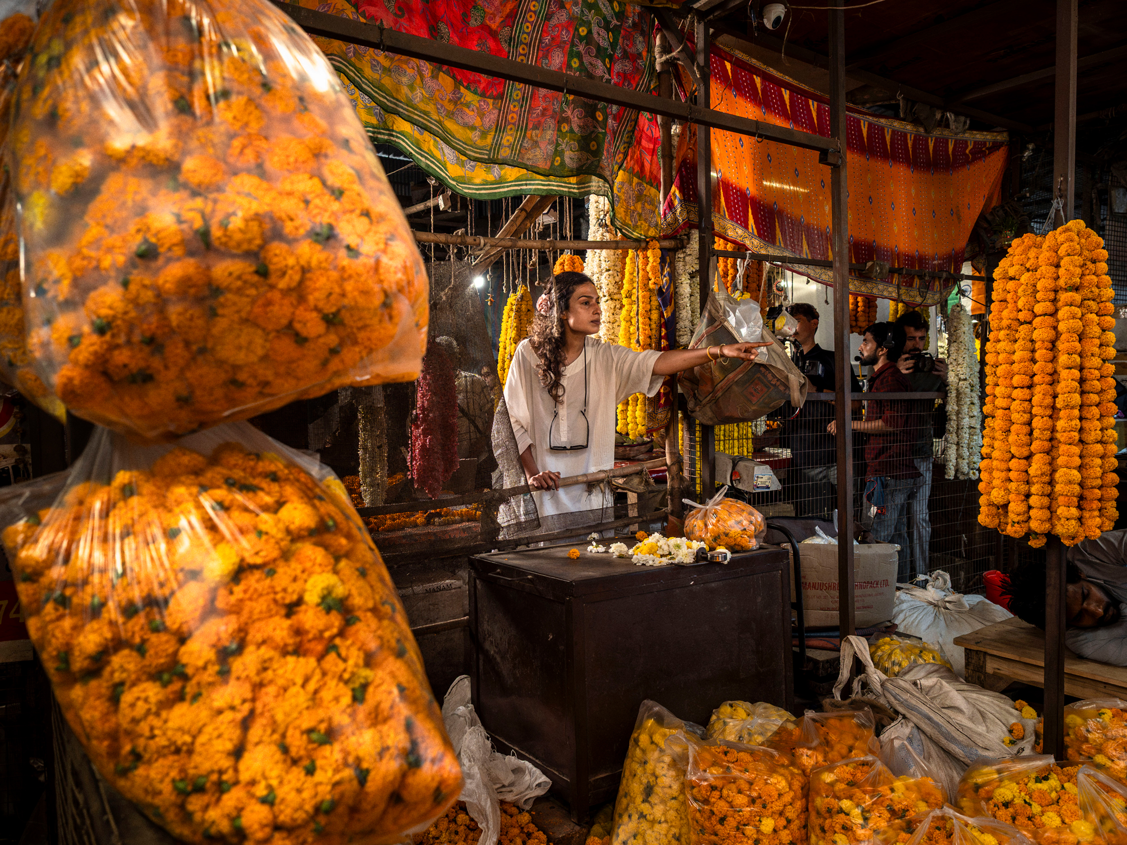 A woman standing in the middle of a market in India, with vibrant orange flowers around her, laying on desk, the floor or hang up in bags