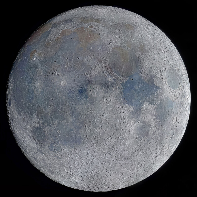 Detailed close-up image of the full moon, showing its craters, maria, and surface textures in shades of gray, with subtle hints of blue and brown under bright illumination against a black background.