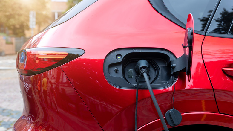 A close-up of a red electric SUV being charged an EV charging station.