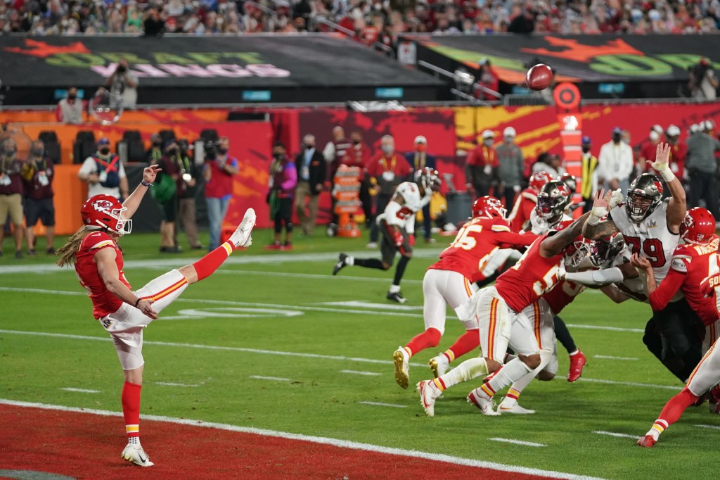 A Kansas City Chiefs player kicks a field goal as the opposing team tries to block it.