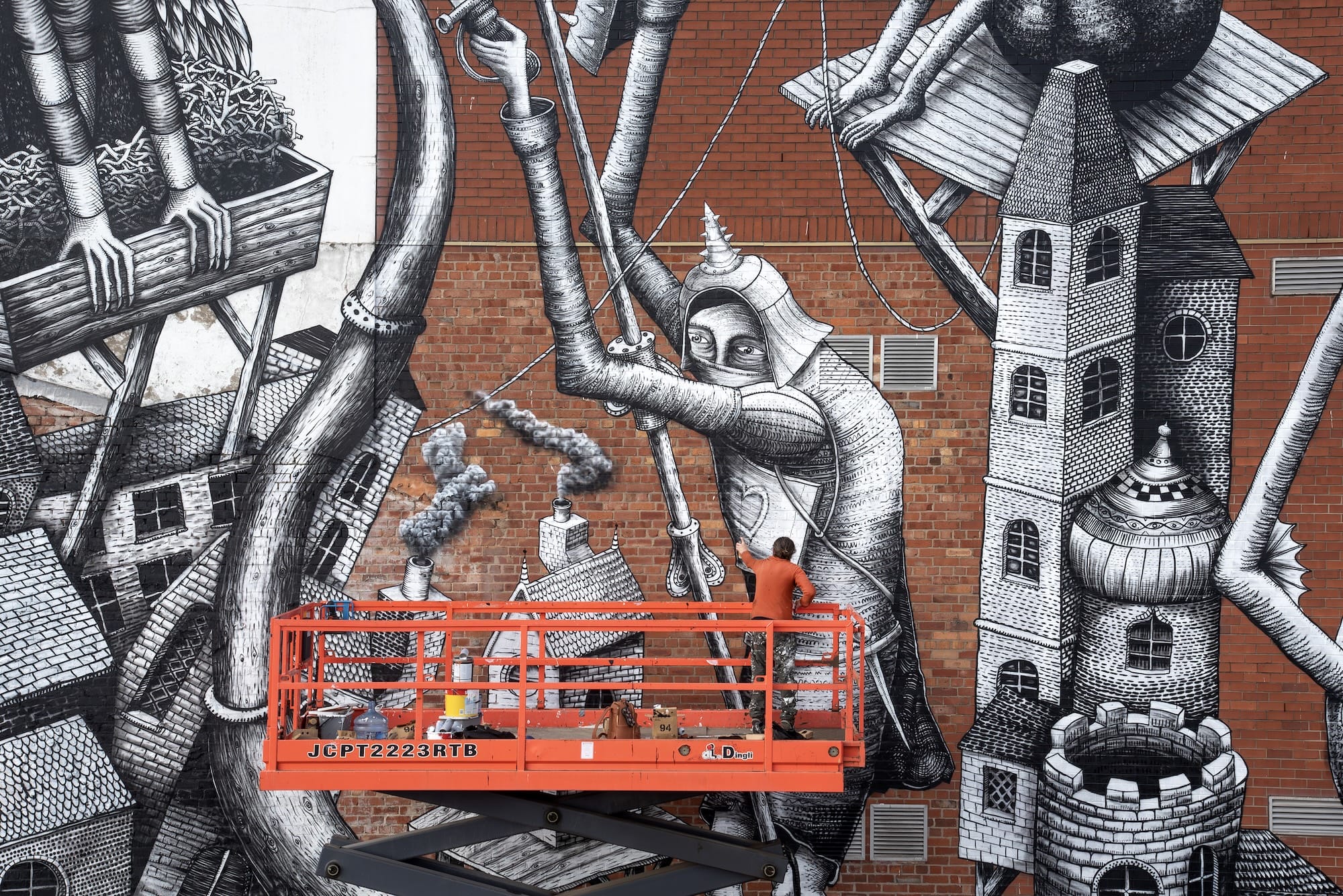 street artist Phlegm works on a mural on the side of a building featuring cartoonish figures and objects merged with lots of different shapes
