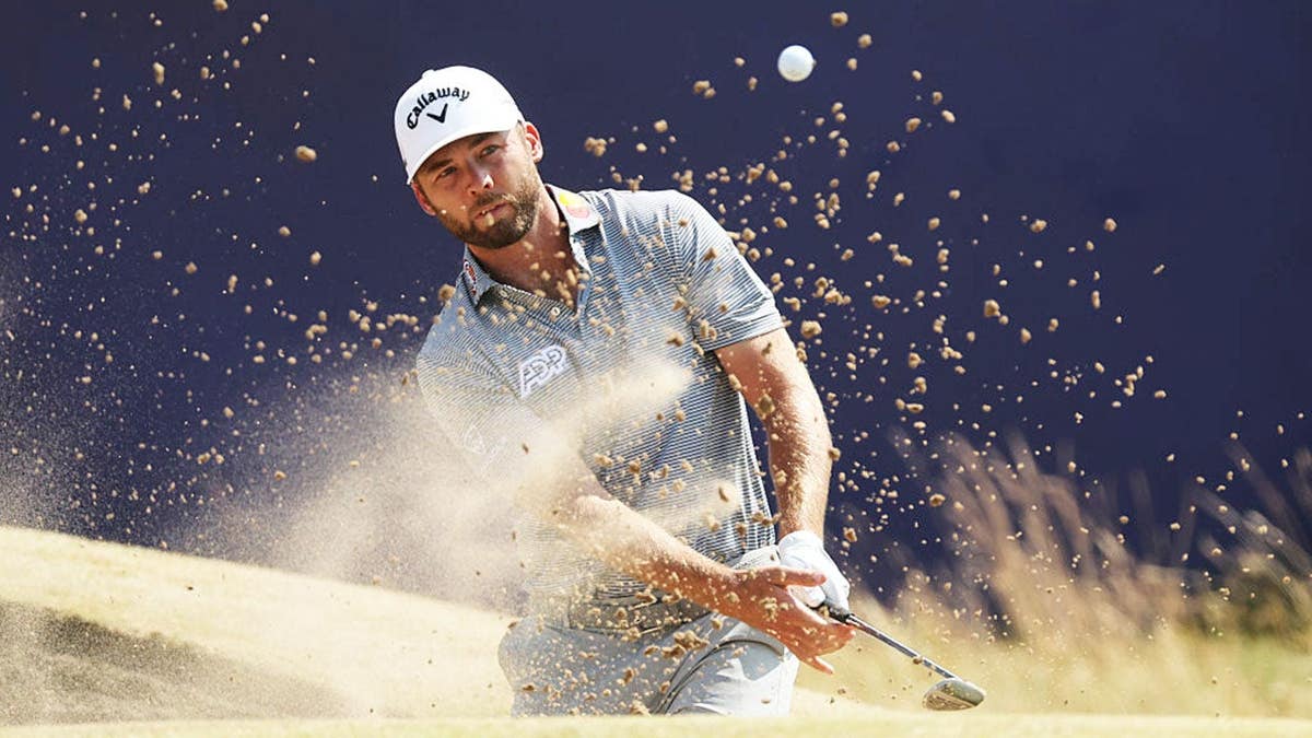 Sam Burns chips from the bunker on the 18th green.