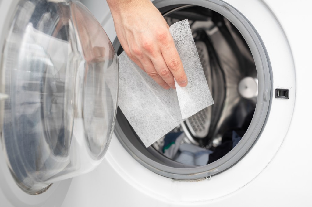 A hand placing a dryer sheet into a washing machine.