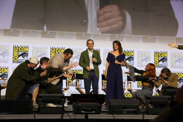 group of actors and producers on stage at San Diego Comic-Com, with many mock bending the knee to a man standing in the center.