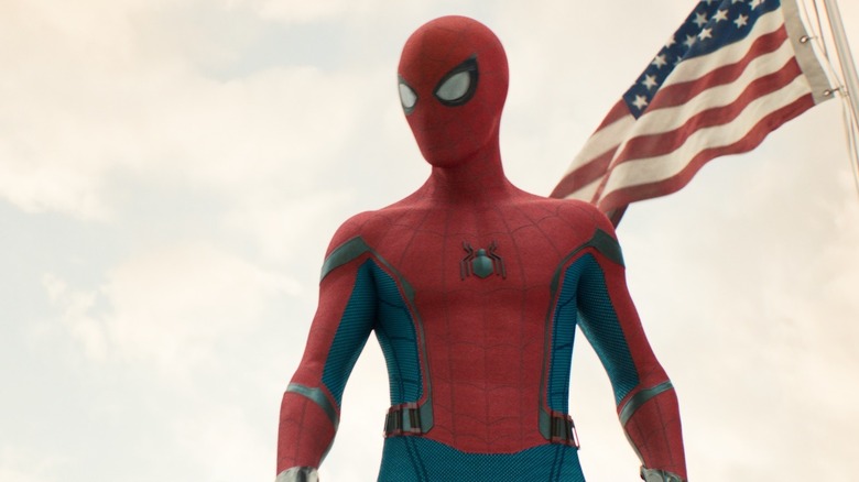 Tom Holland as Peter Parker wearing his superhero suit and standing by an American flag in Spider-Man: Homecoming