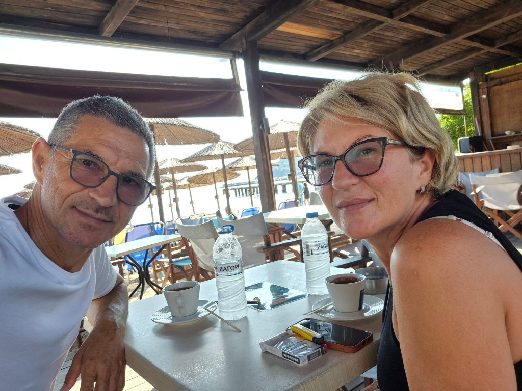 Svetlana Grkovic and Ljubisa Karovic sitting at a table with coffee and water bottles, beach umbrellas in the background.