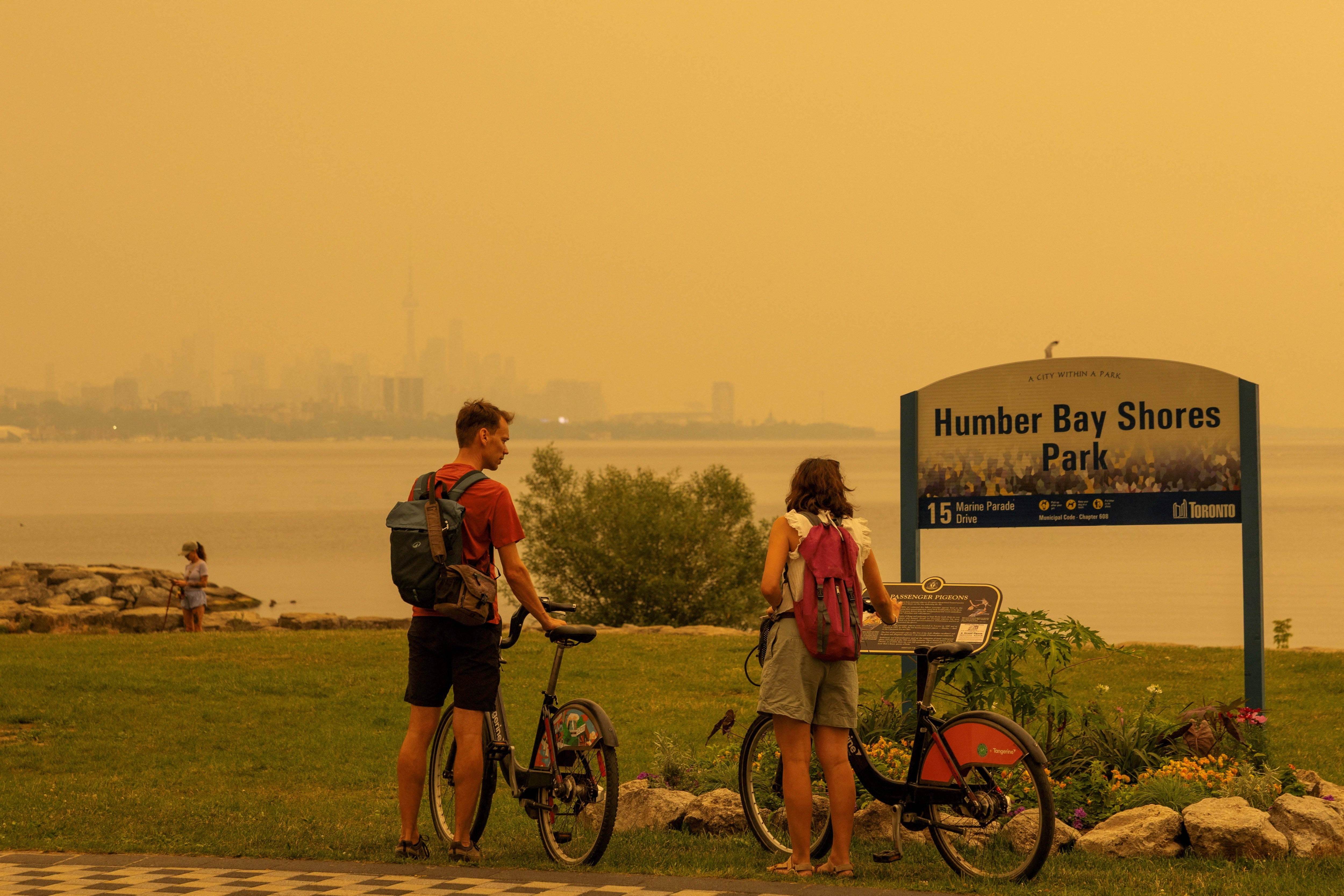 Two people read a sign at a park as wildfire smoke from northwestern Ontario fills the sky in Toronto, Canada, on Wednesday. Hundreds of Canadian wildfires are sending choking smoke across provinces and into the U.S.