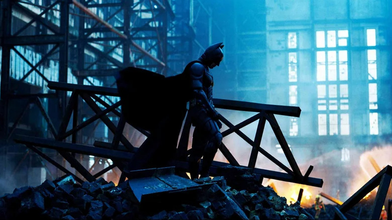 Batman looking down at some debris and pondering whether his crusade was worth it in The Dark Knight