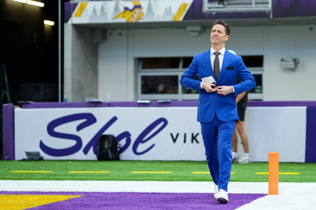 A man in a blue suit walks on a football field.