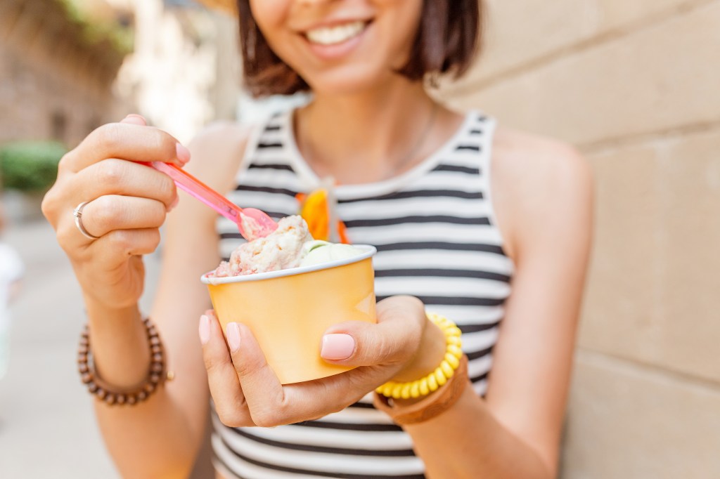 A happy woman in a straw hat and striped top smiles while holding a cup of ice cream.