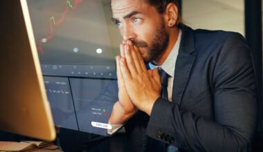 Person in a suit looking at a computer screen with folded hands.