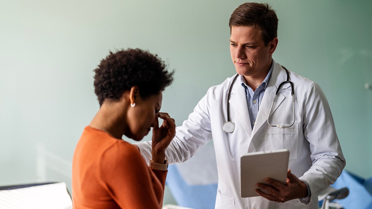 Doctor consoles woman during check-up as she holds head in apparent distress or pain
