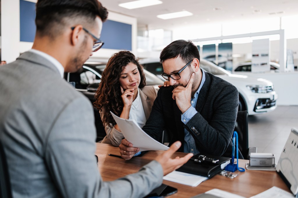 A salesman sitting across the table from a worried middle-aged couple in a car showroom.