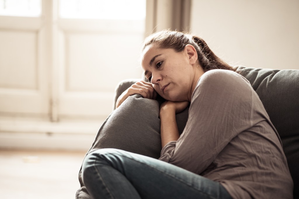 A young woman sits on a couch looking sad and lonely, suffering from depression.