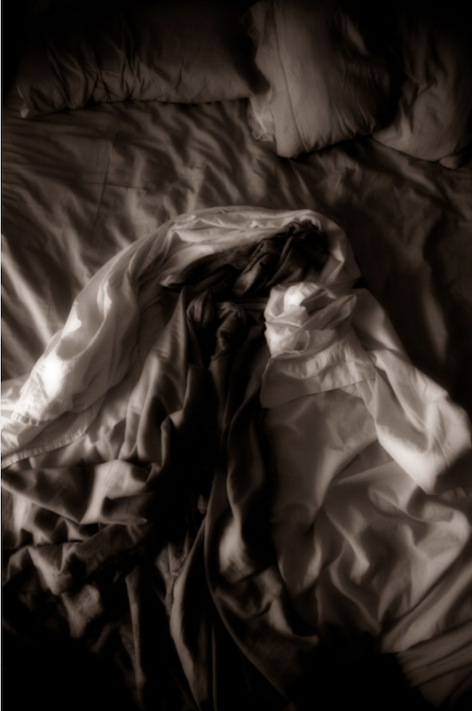 A dark, blurred black-and-white image of rumpled bedding, © Ann Mitchell.