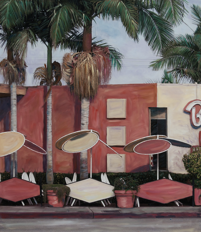 A red building with palm trees, umbrellas, and patio seating in front, © Ann Mitchell.