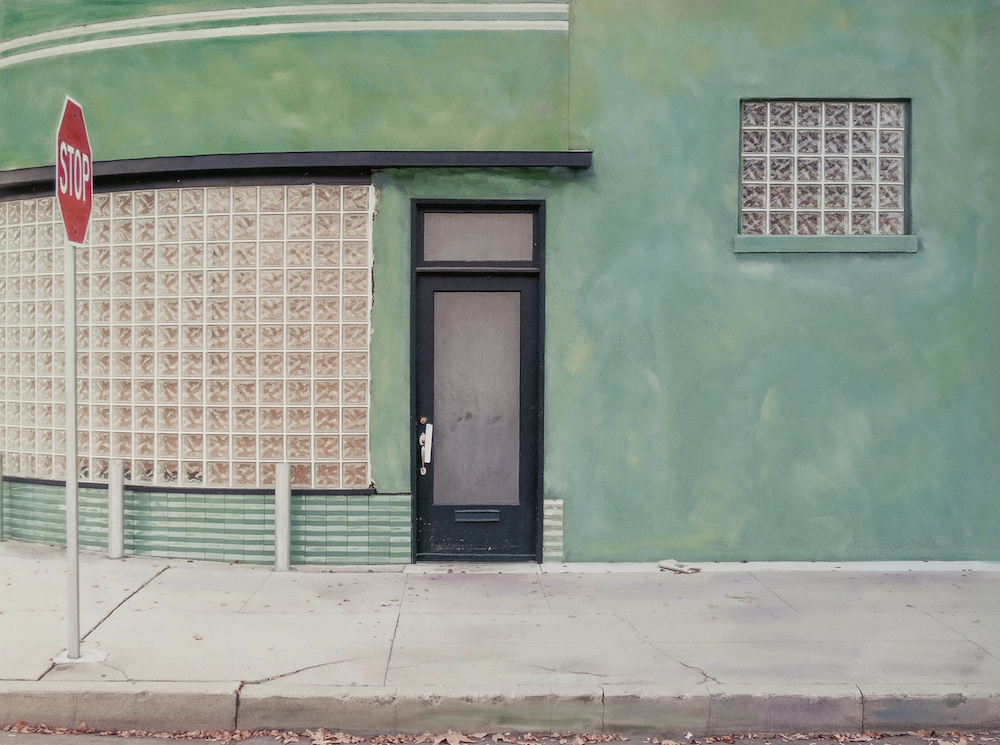 A quiet street view of a green building façade with a dark door and tiled wall, © Ann Mitchell.