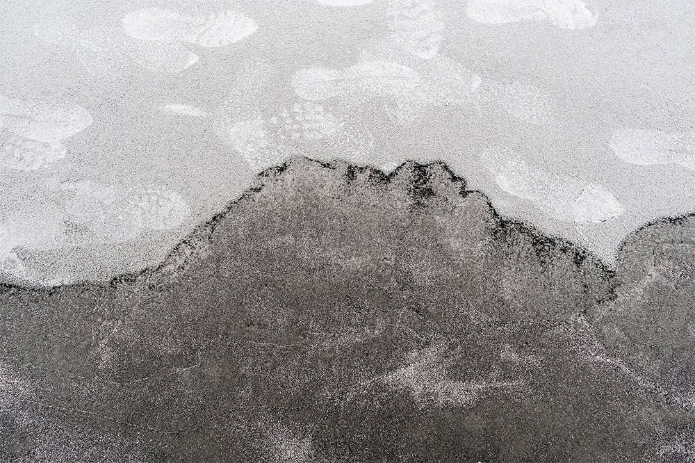 Dark wet sand meets pale, foamy water in a high-contrast abstract shoreline resembling a distant mountain range. ©CynthiaGladis