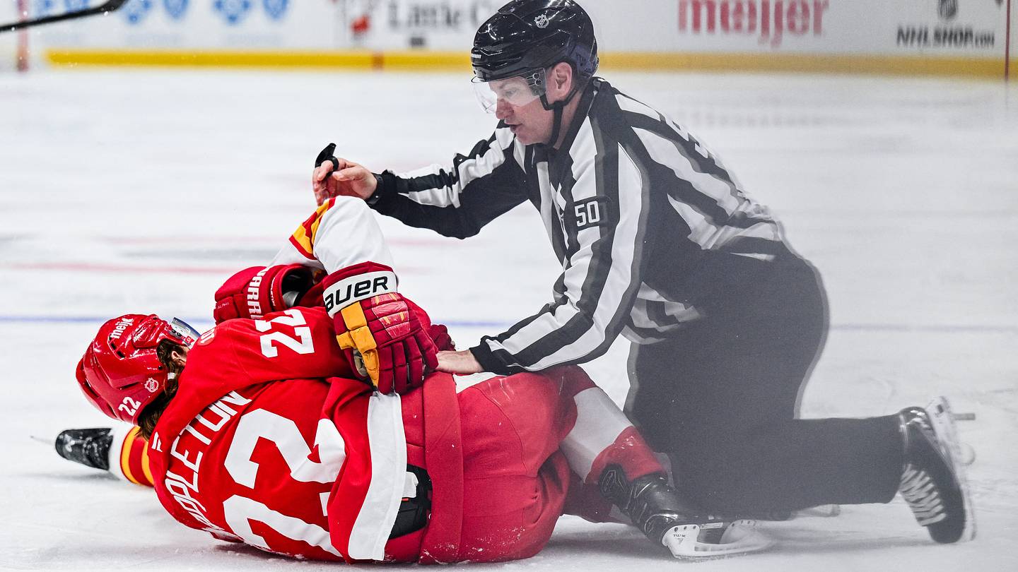 Mar 16, 2026; Detroit, Michigan, USA; Detroit Red Wings center Mason Appleton (22) and Calgary Flames center Connor Zary (47) are broken up by linesman Scott Cherrey (50) during the second period at Little Caesars Arena. Mandatory Credit: Tim Fuller-Imagn Images