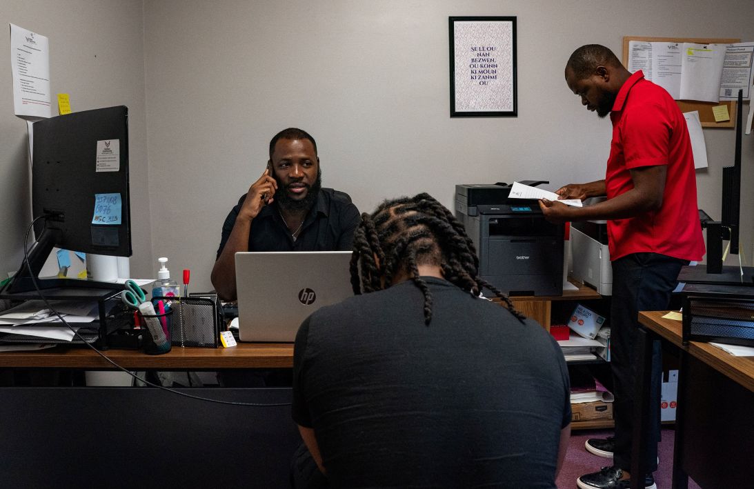 James Fleurijean, administrative assistant at the Haitian Community Help and Support Center in Springfield, helps a Haitian immigrant on August 3 before his mandatory immigration check-in later in the week as Dorsainvil, right, reviews paperwork for another case.