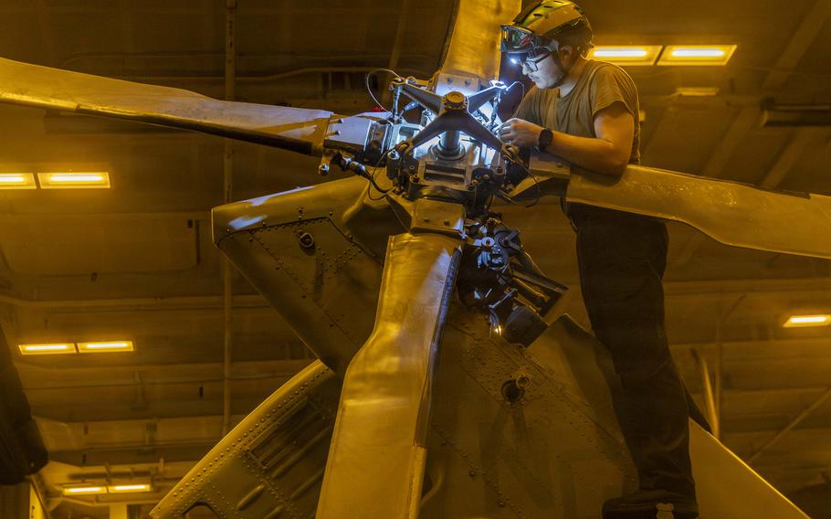 A sailor working on a helicopter rotor in a ship’s hangar bay.