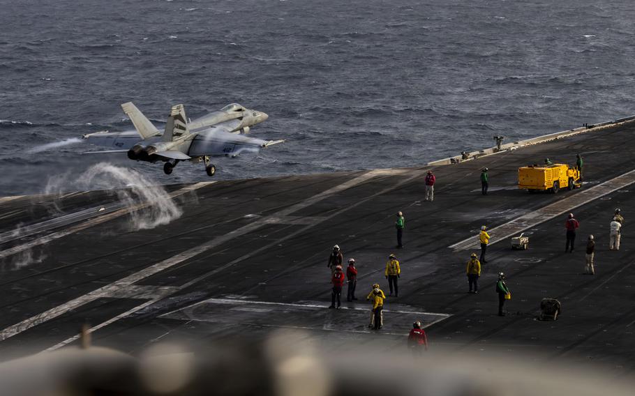 A fighter jet launching from an aircraft carrier flight deck over the ocean. 