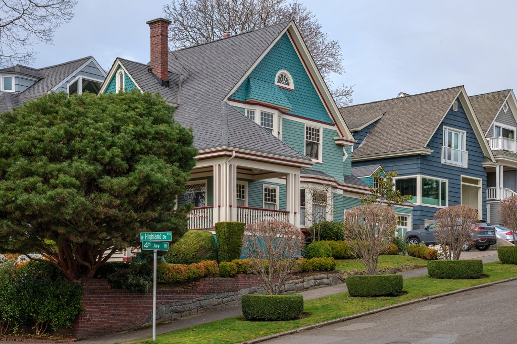 A green single-family home in the distance with a green street sign in the foreground. 